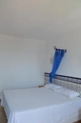 a bedroom with a white bed with a blue curtain at Oasis en la playa: piscina y relax in Cullera