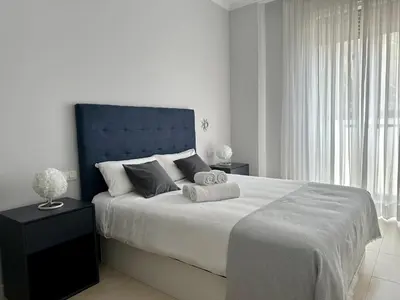 a white bedroom with a large bed with a blue headboard at Reinapart Patacona Beach 36 in Valencia