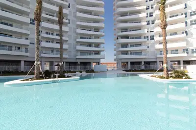 a swimming pool with palm trees in front of a building at Global Vacacional, Moderno apartamento con 2 terrazas y 3 habitaciones in Canet de Berenguer
