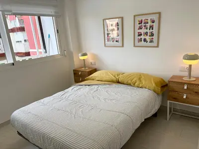a bed in a bedroom with two night stands and a window at Escápate al Sol Apartamento con Piscina y Playa Cercana in Playa Pobla de Farnals