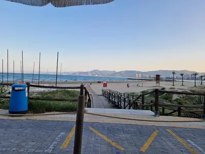 a beach with a blue trash can and a fence at Apartamentos Bon Amb in Faro de Cullera