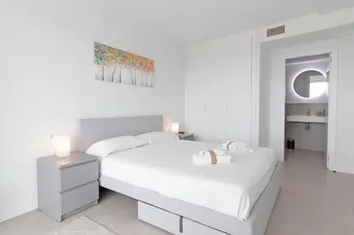a white bedroom with a bed and a mirror at Global Vacacional, Apartamento con terraza, vistas al mar y a la piscina in Canet de Berenguer