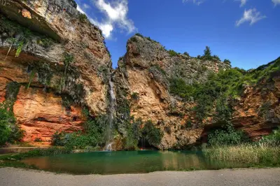 a waterfall on the side of a mountain with a pond at LA TRAVIATA - Buñol in Buñol