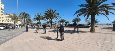 a group of people standing on a sidewalk next to palm trees at Latido Del Puerto in Puerto de Sagunto