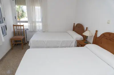 a bedroom with two beds and a chair and a window at Solimar, 4-8 in Cullera