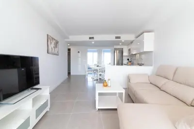 a white living room with a couch and a tv at Global Vacacional, Apartamento con 2 terrazas en Gran Canet in Canet de Berenguer