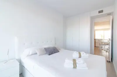 a white bedroom with a large white bed with two towels at Global Vacacional, Apartamento con 2 terrazas en Gran Canet in Canet de Berenguer