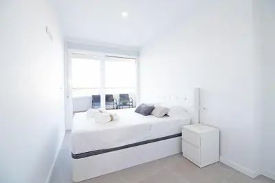a white bedroom with a white bed and a window at Global Vacacional, Apartamento con 2 terrazas en Gran Canet in Canet de Berenguer