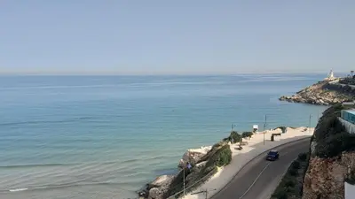 a road next to the ocean with a car on it at Faro Cullera primera Linea Playa del Dosel in Faro de Cullera