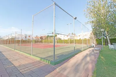 a tennis court with a net in a park at Global Vacacional, Adosado con piscina en la playa de Canet in Canet de Berenguer