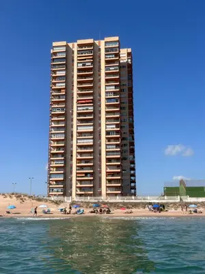 a tall building on the beach with people on the beach at Mareny de Barraquetes in Mareny Blau