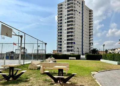 a park with two picnic tables and a tall building at Mareny de Barraquetes in Mareny Blau