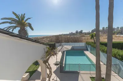 a swimming pool with an umbrella and palm trees at Exquisita Villa Frente al Mar in Sagunto