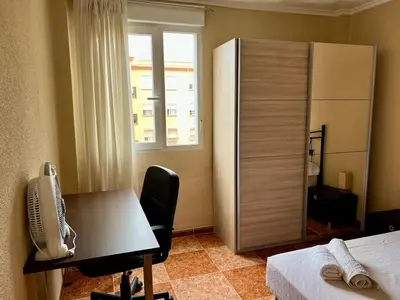 a room with a desk and a refrigerator and a bedroom at Bonito y grande apartamento cerca de la playa in Valencia