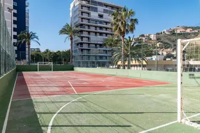 a tennis court with palm trees and a building at Florazar I frente a la playa in Cullera