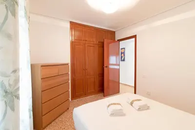 a bedroom with a white bed and a wooden cabinet at Global Vacacional, Apartamento céntrico en Puerto de Sagunto para 5 personas in Puerto de Sagunto