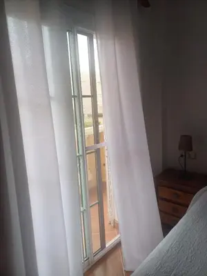 a bedroom with a window with white curtains at Adosado/casa con terraza y buhardilla. Playa El Perelló in El Perelló