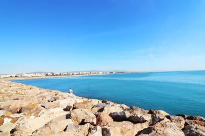 a man sitting on a rocky shoreline near the water at Global Vacacional, Práctico apartamento muy cerca del mar en Puerto Sagunto in Puerto de Sagunto