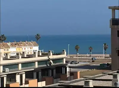a building with a parking lot with palm trees and the ocean at Piso acogedor con vistas al mar in La Torre