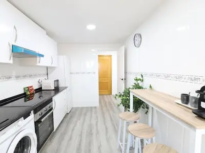 a white kitchen with a counter and stools in it at Esplendido apartamento para 6 personas by Hometels in Puerto de Sagunto