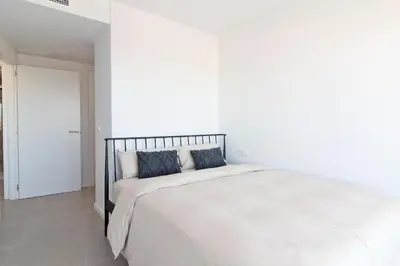 a white bedroom with a large white bed at Global Vacacional, Moderno apartamento de dos terrazas con increíbles vistas al mar in Canet de Berenguer