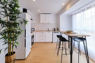 a kitchen with white cabinets and a wooden table and stools at REINA FLAT in Valencia