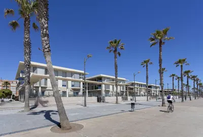 a man riding a bike past a building with palm trees at Patacona Mediterranean Beach in Valencia