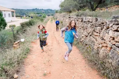 two girls walking down a dirt road next to a stone wall at La casita del Horno in Pedralba