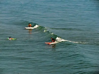 three people riding a wave on surfboards in the ocean at Apartamento ARENSOL EN PRIMERA LINEA DE PLAYA in Cullera