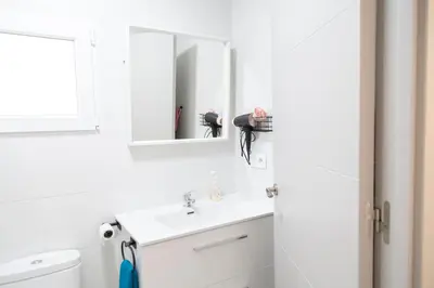 a white bathroom with a sink and a mirror at El hogar del mar. in Sueca