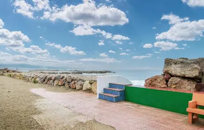 a bench next to a beach with rocks and the ocean at Beautiful Apartment In Cullera in Cullera