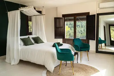 a bedroom with a bed and two green chairs at Masia de Matuta in Vall de Almonacid