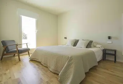 a white bedroom with a large bed and a chair at La Casa del Mar in Valencia