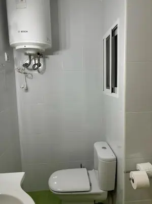 a white bathroom with a toilet and a water tank at Acogedor Apartamento Cullera 200 metros playa in Cullera