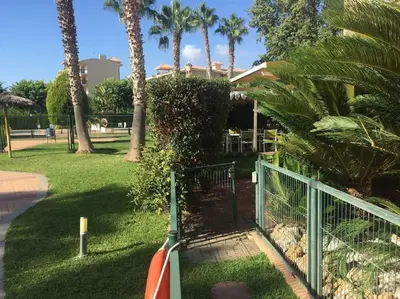 a gate in a park with palm trees and grass at Agradable adosado con piscina y jardín in Canet de Berenguer