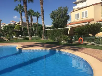 a swimming pool in front of a building with palm trees at Agradable adosado con piscina y jardín in Canet de Berenguer