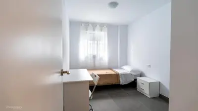 a small white bedroom with a bed and a window at Apartamentos Borriana in Burriana