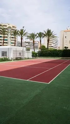 a tennis court with palm trees and a building at Apartamento en complejo residencial con piscina in Puebla de Farnals