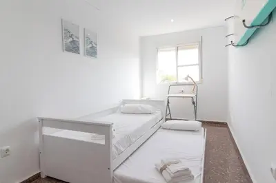 a white room with two beds and a window at Global Vacacional, Bonito apartamento en Puerto de Sagunto cerca de la playa in Puerto de Sagunto