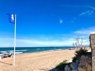 a beach with a flag in the sand and the ocean at Vacaciones con el Mediterráneo a menos de 50 metros in Cullera