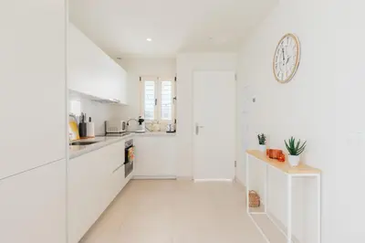 a white kitchen with white cabinets and a clock on the wall at Terrasses - Beach apartment with swimming pool in Puzol