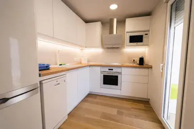 a white kitchen with wooden floors and white cabinets at Apartamento acogedor en la Playa de Nules in Nules