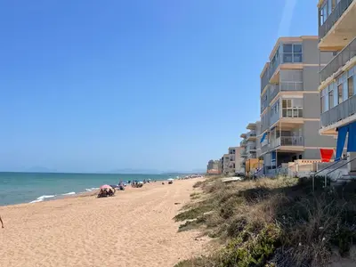 a sandy beach with a building and the ocean at ESTUDIO CON JACCUZI Y SAUNA montaña y playa in Tavernes de Valldigna