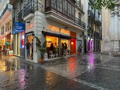 a wet city street with people walking in front of a store at Turia Gardens Rooms - Authentic Valencia Downtown Parklife - VLC Urban Rental in Valencia