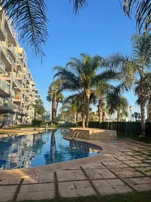 a swimming pool with palm trees and a building at Apartamento en Moncofa in Moncófar
