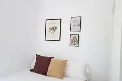 a white couch with three framed pictures on a white wall at 2 apartamentos en una excelente villa de playa compartiendo Piscina y Jardín in Sagunto