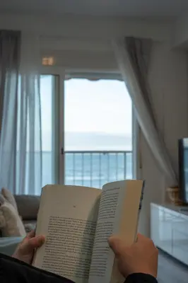 a person is reading a book in a living room at 1ª Linea de Mar 4pax Valencia 15 min in El Perellonet