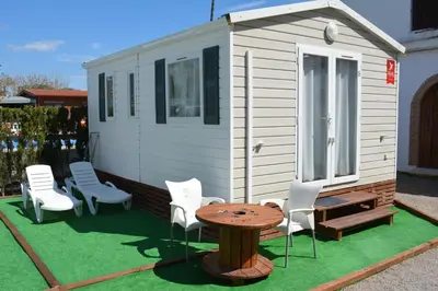 a tiny house with white chairs and a table at Camping Valencia el Saler in El Saler