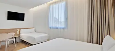 a hotel room with a bed and a chair and a window at B&B HOTEL Valencia Alcàsser in Alcácer