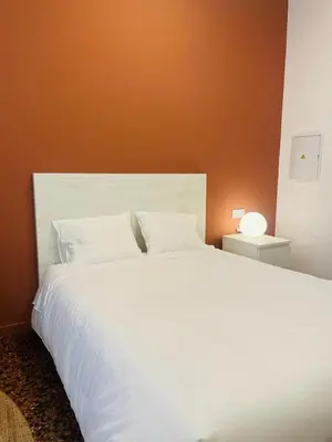 a bedroom with a white bed with an orange wall at Apartahotel Espai Verd Benimaclet in Valencia